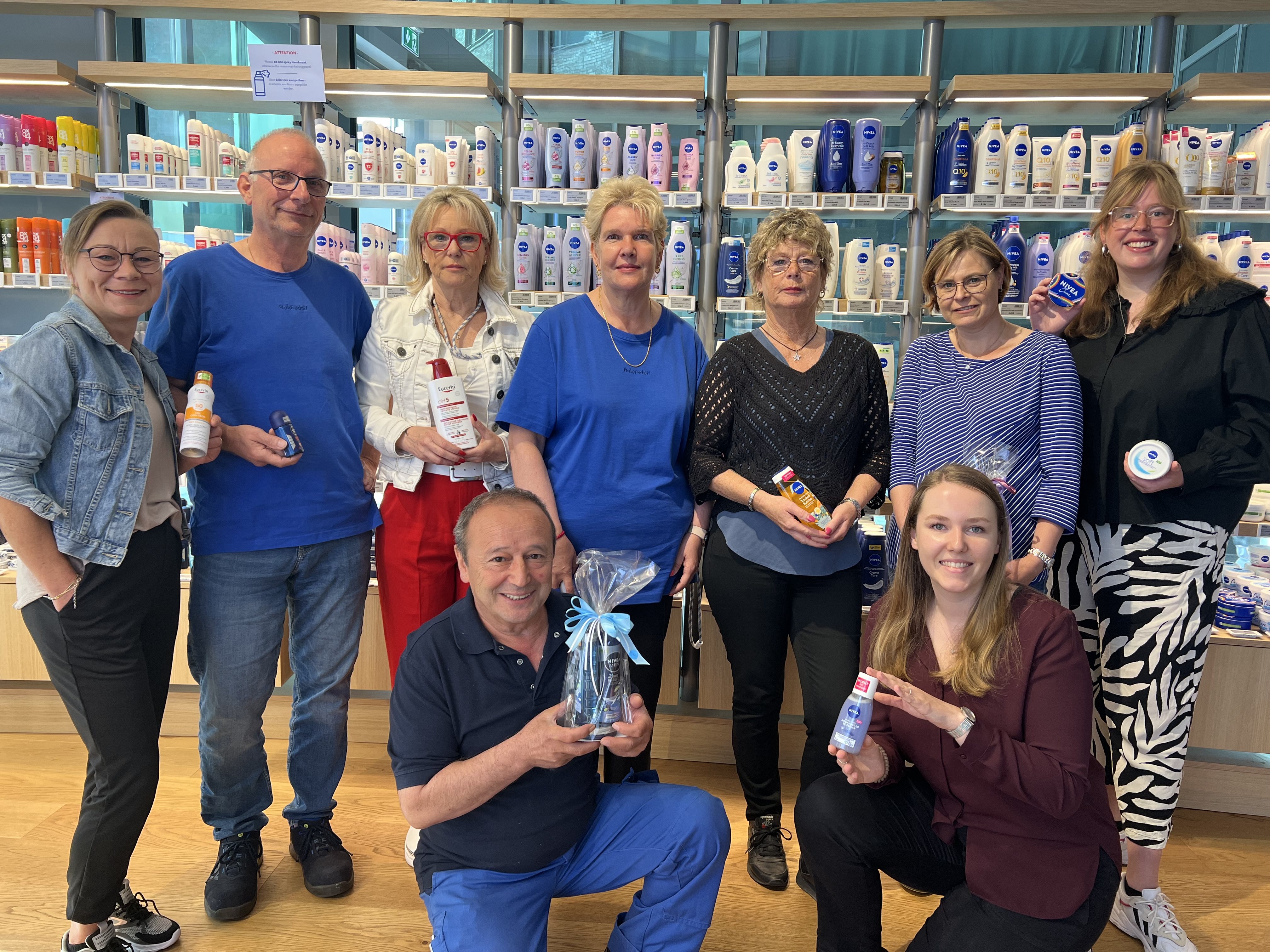 Group of people posing together indoors in front of shelves filled with products, smiling and holding small items.