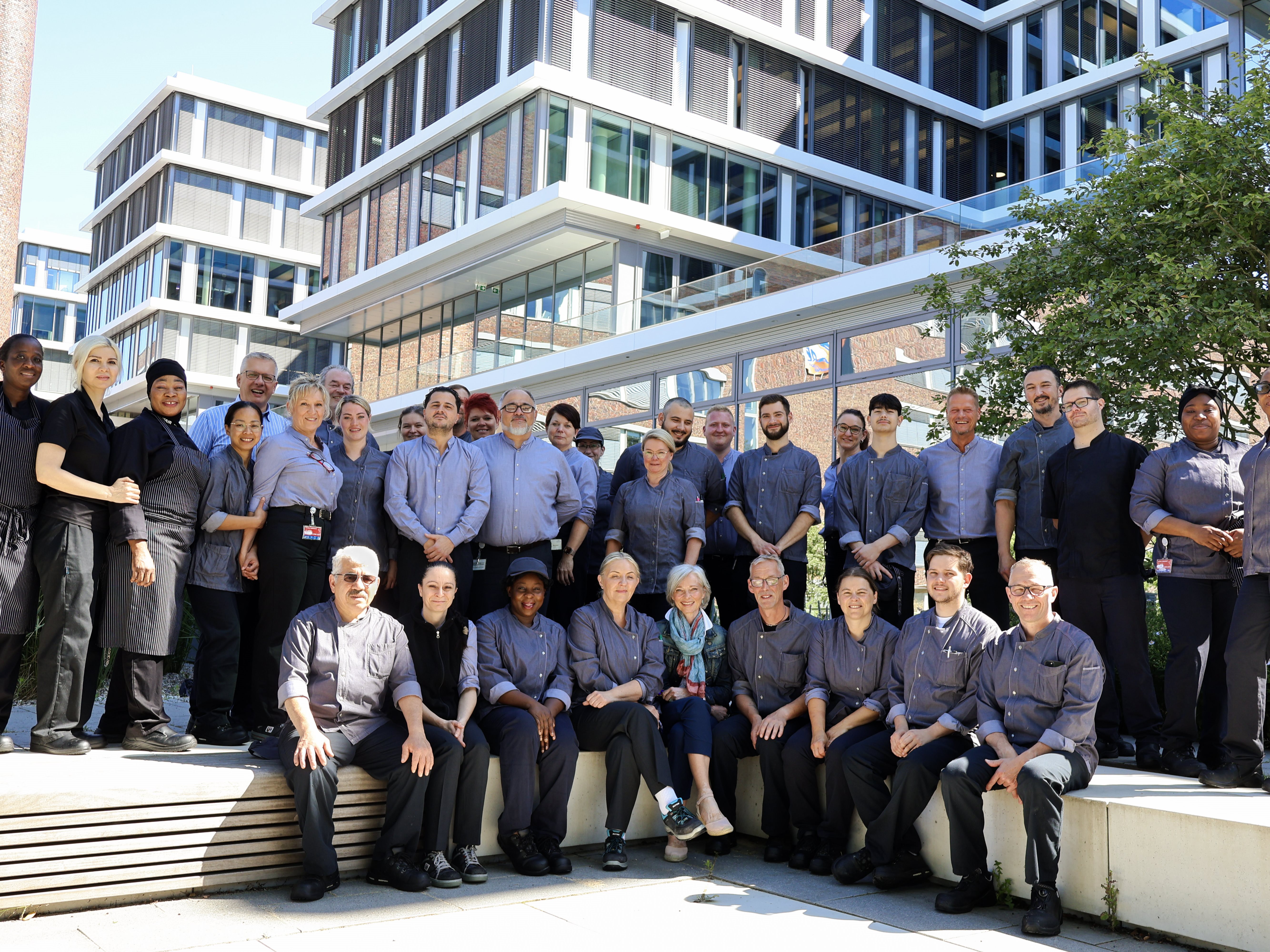 Large group of people gathered outdoors in front of a modern building, posing together for a group photo.