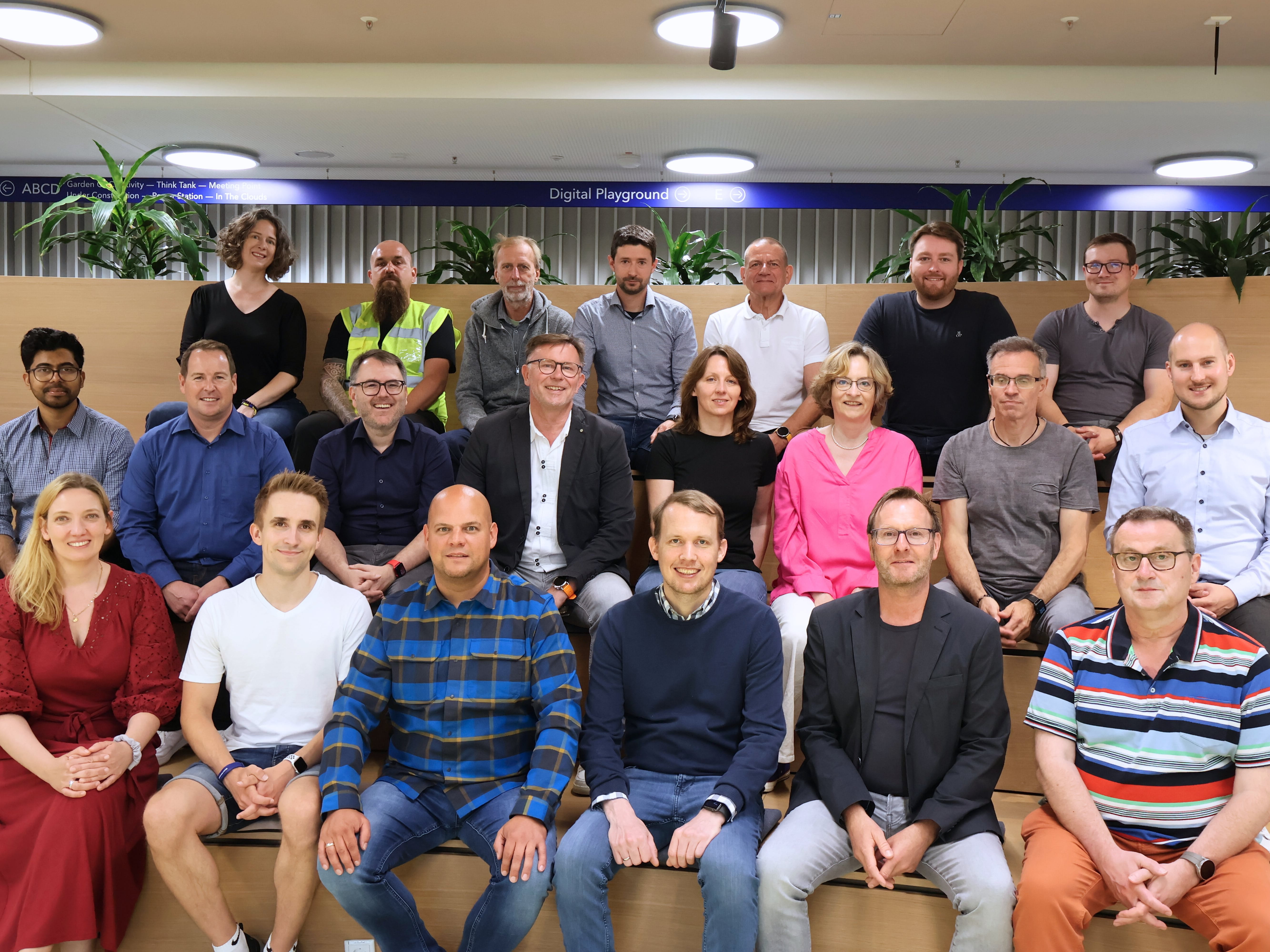Large group of people seated and standing indoors in a lecture or classroom setting, posing together and smiling.