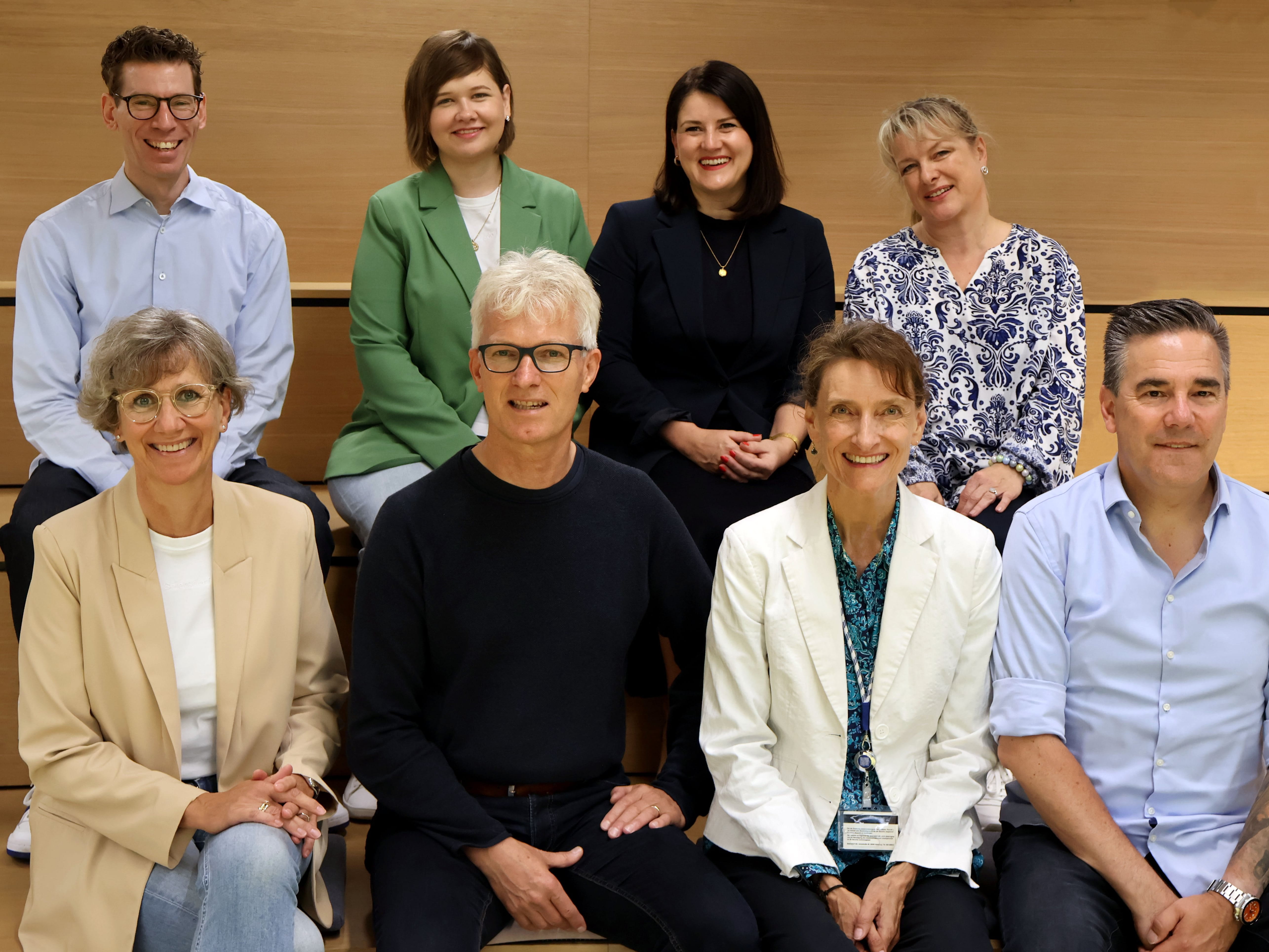 Group of people seated and standing indoors in a lecture or meeting space, posing together and smiling.