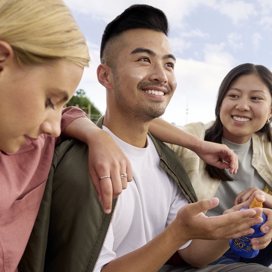 Three people sitting outdoors, smiling and talking together, with one person holding a small snack or object in their hand.