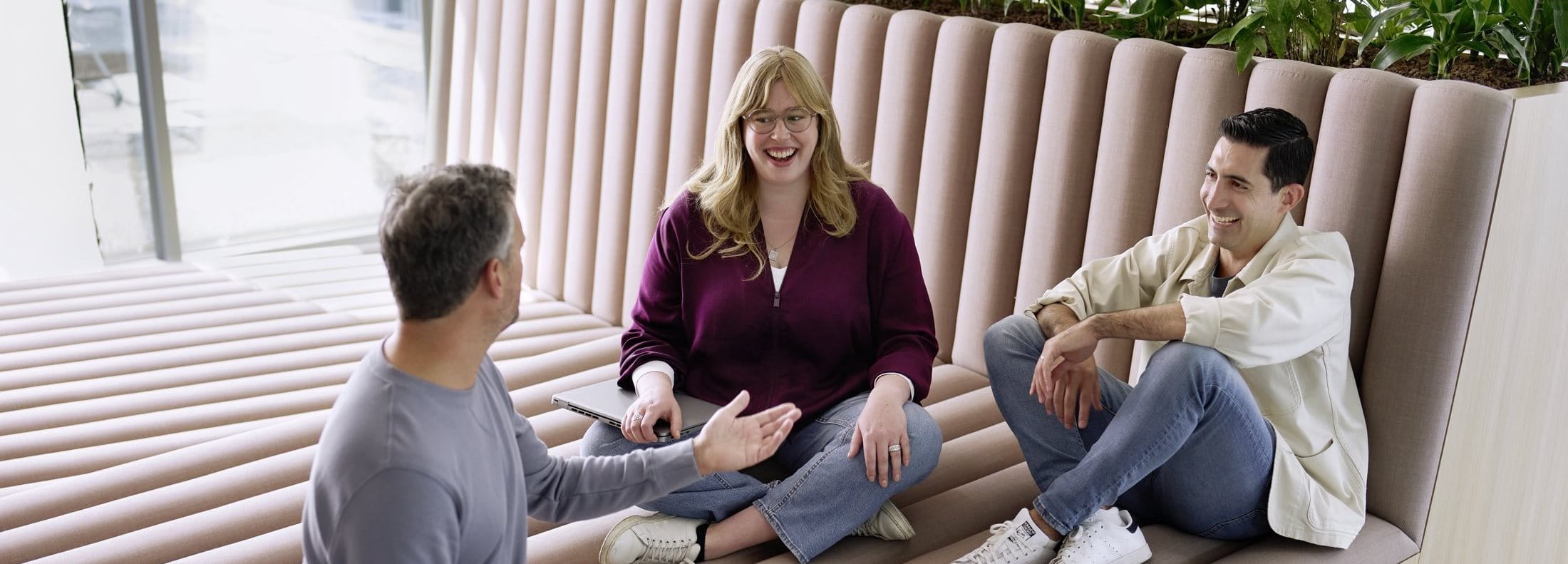 Three people sitting together in a casual seating area, talking and smiling during a relaxed group conversation.