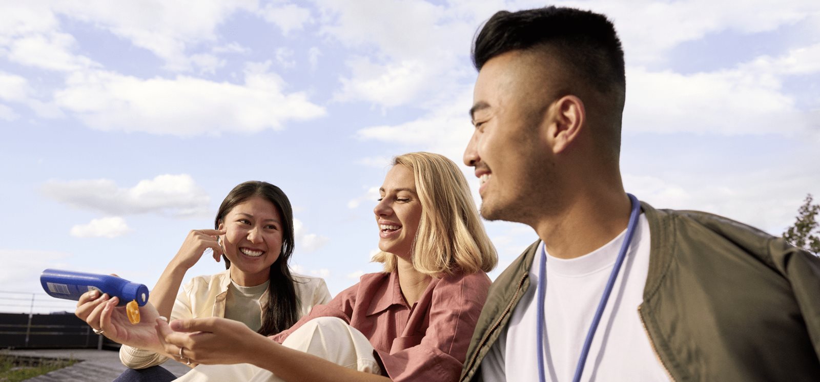 Group of friends sitting outdoors, smiling and chatting together during a relaxed social moment.