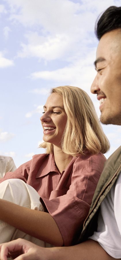 Young woman smiling while holding a sunscreen bottle outdoors, enjoying a sunny day with a relaxed expression.