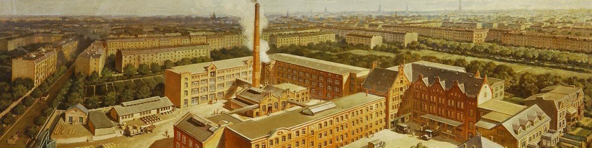 Historic panoramic view of an industrial factory complex with multiple buildings and chimneys, set within an urban landscape.