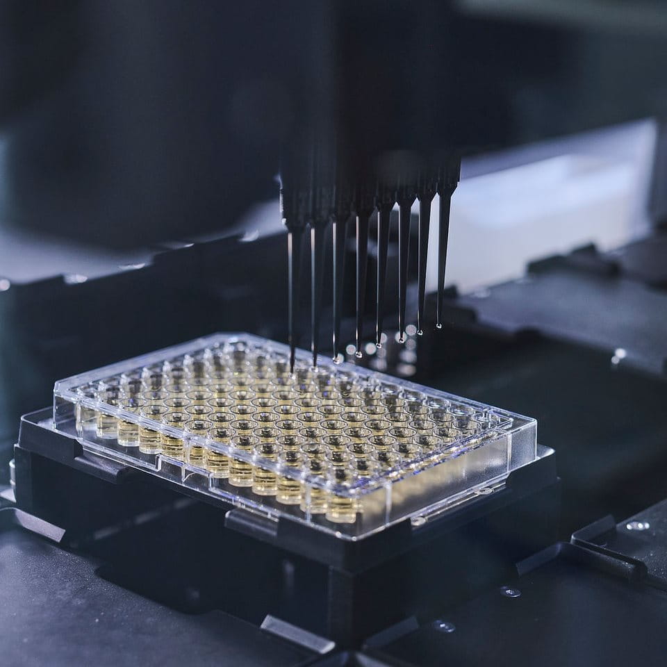 Automated laboratory pipetting system dispensing liquid into a multiwell plate, illustrating high-throughput scientific testing and analysis.