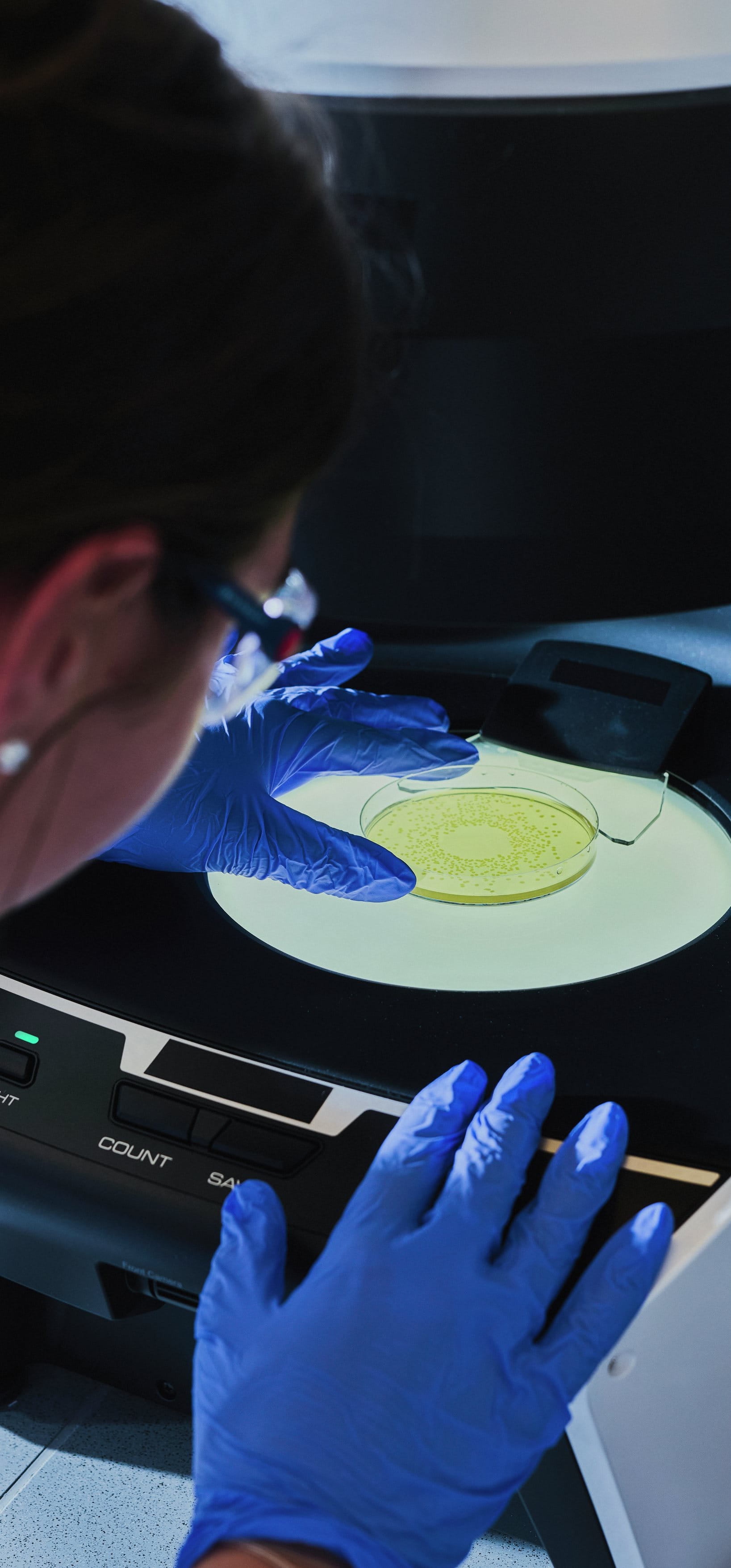 Scientist wearing blue gloves placing a sample dish into a laboratory analysis device, carefully positioning it for testing.