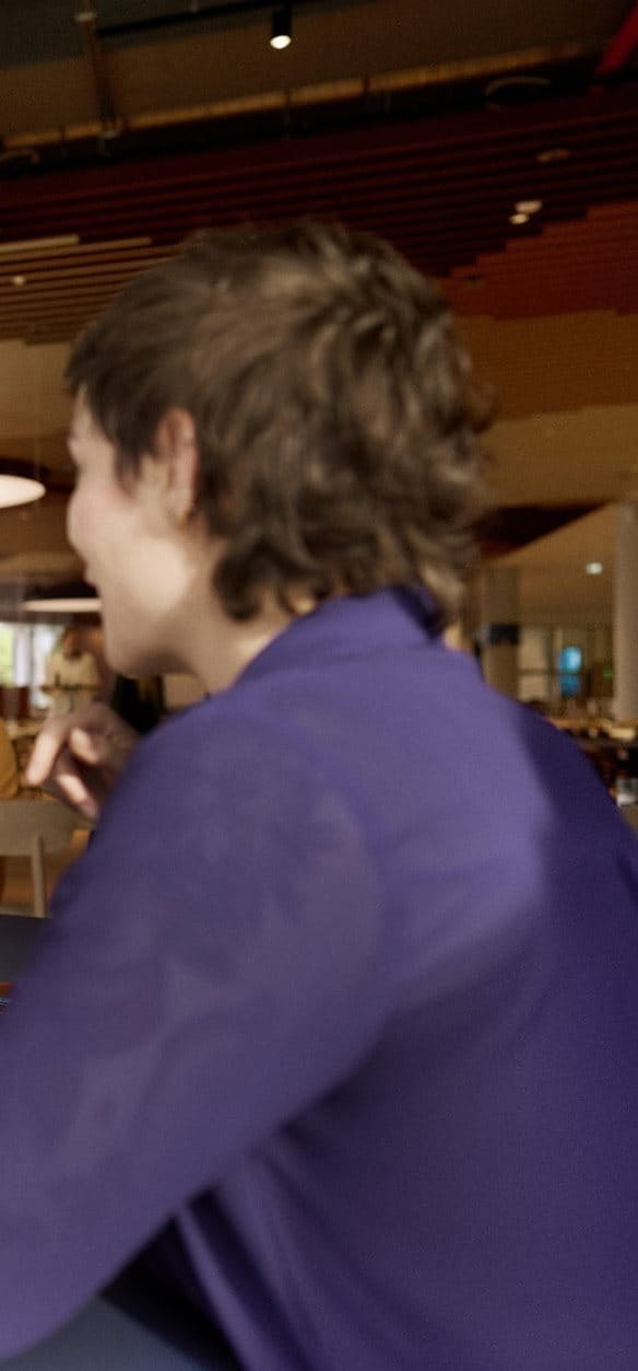 Two people seated at a table in a modern café or communal space, talking and smiling during a relaxed conversation.