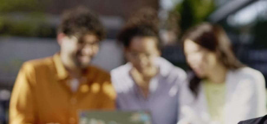 Three people standing close together in conversation outdoors, with faces softly blurred to convey a casual, social interaction.