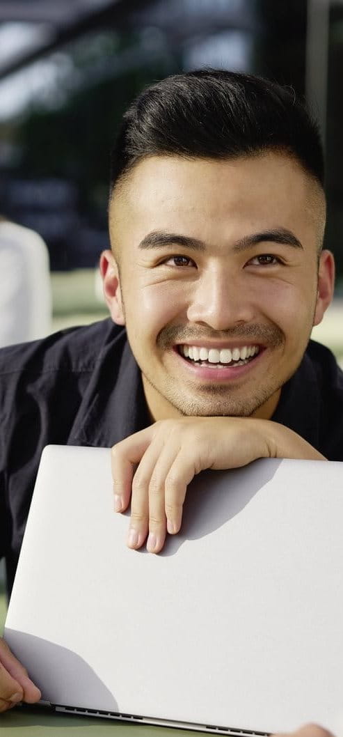 Young man smiling while speaking with a colleague during a group discussion, holding a folder in a bright indoor workspace.